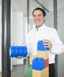Tobias Otten Geschäftsführer der Schneider Immobilien GmbH zeigt mit großen Legosteinen, dass er auch als Vater gerne baut.