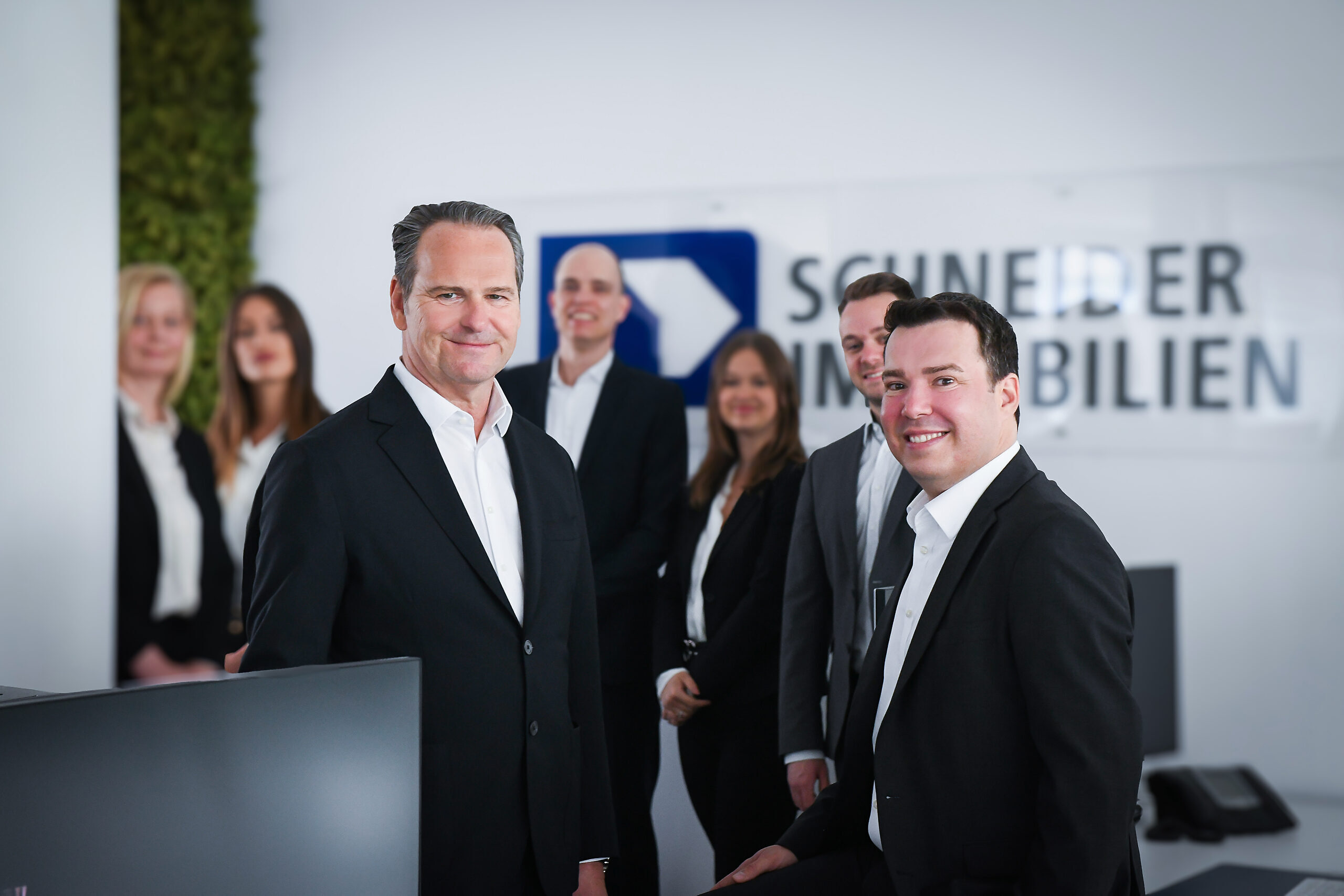 Geschäftsführung Schneider Immobilien mit Team im Hintergrund
